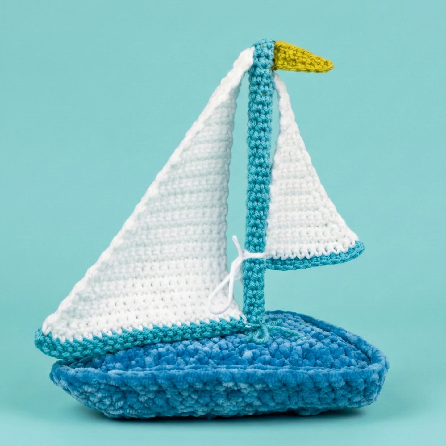 crochet sailboat plushie with white sails and blue base on light blue background