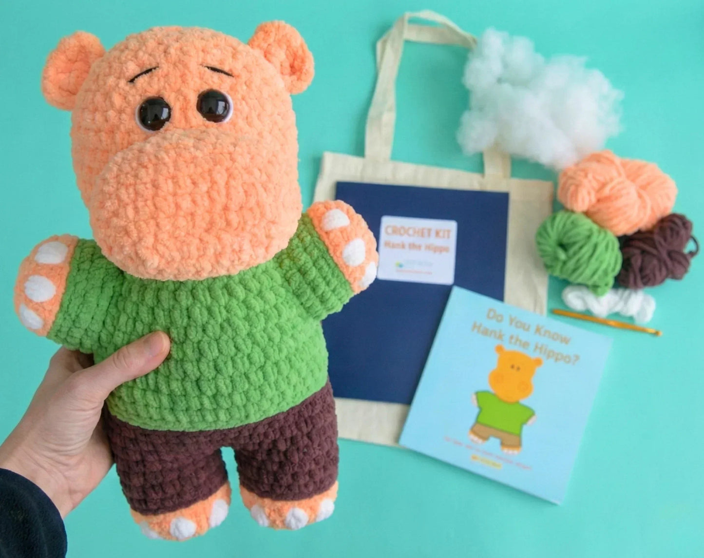 Beginner-friendly crochet hippo plushie kit with yarn, stuffing, book, hook, and tote bag.