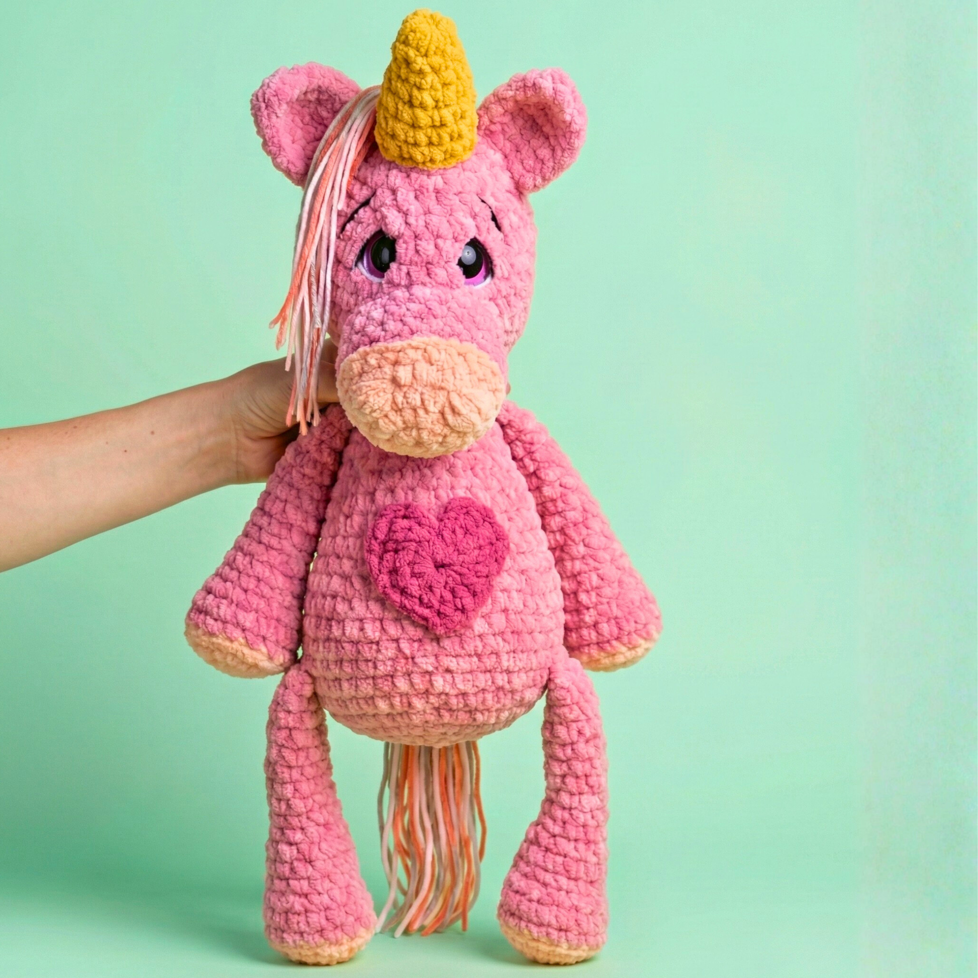 Pink crochet unicorn with a yellow horn on a green background