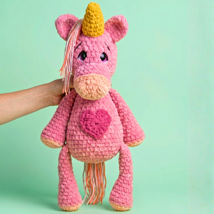Pink crochet unicorn with a yellow horn on a green background